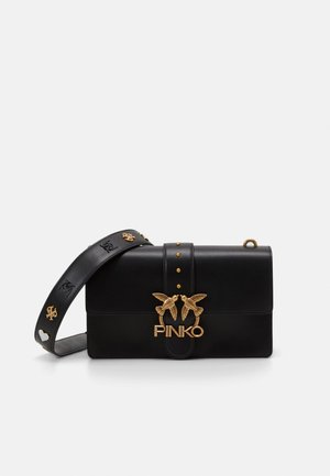 Sac à bandoulière en cuir noir avec fermoir doré en forme d'oiseau et clous décoratifs, avec une large sangle embossée de symboles.