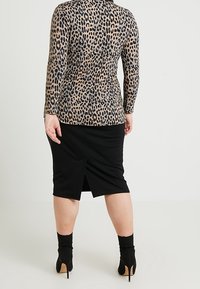 Langärmliges Oberteil mit Leopardenmuster in taillierter Silhouette, kombiniert mit einem schwarzen knielangen Rock mit Schlitzausschnitt hinten, getragen mit schwarzen High Heels.
