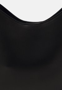Černá hladká kožená kabelka s kulatým horním okrajem, bezešvým designem a jemným prošíváním podél okrajů, což jí dodává elegantní vzhled.