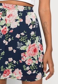 Saia floral azul-marinho com rosas cor-de-rosa e verdes, tecido leve, design pregueado e faixa elástica na cintura. Acentuada com pequenas flores brancas.
