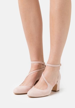 Chaussures à talons blocs en daim rose avec un design découpé ouvert, comportant des sangles de cheville et un décor croisé. Les talons sont épais pour plus de stabilité.