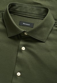 Košulja maslinaste boje sa uzorkom, sa raširenim ovratnikom, bijelim dugmadi i crnom etiketom s natpisom "Matinique" na vratu.