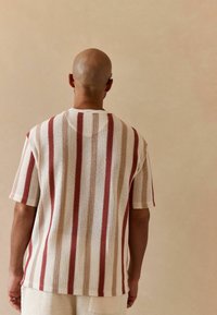 T-shirt med kortærmer, strikket i en løs pasform. Har skiftende røde og cremefarvede horisontale striber. Tekstureret stof, rund halsudskæring.