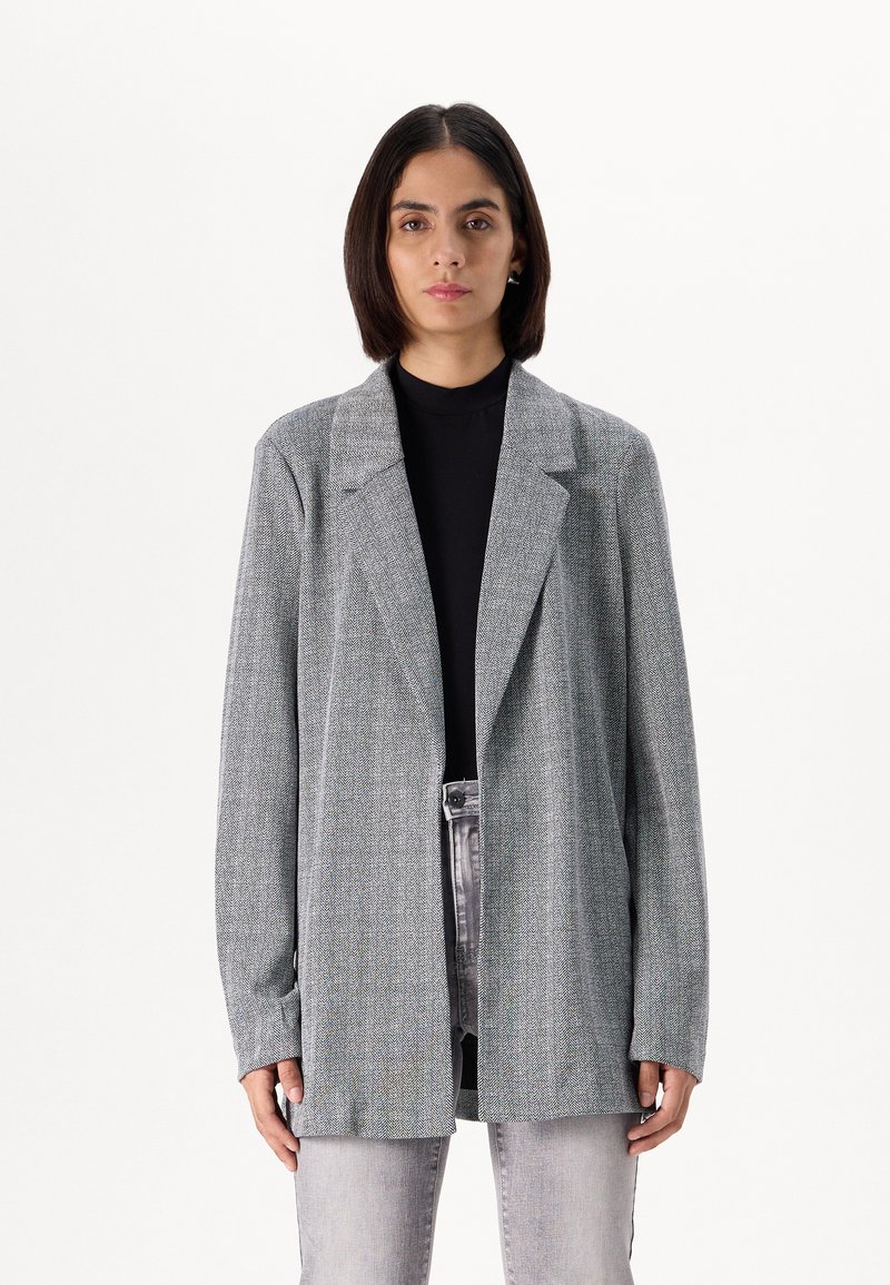 Light gray blazer with a textured weave, notched lapels, and long sleeves, worn over a black top and paired with gray jeans.