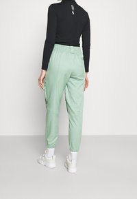 Joggingbroek in muntgroen met elastische tailleband en boorden, voorzien van zijzakken en een matte, gladde textuur. Draagt een zwarte top met lange mouwen.