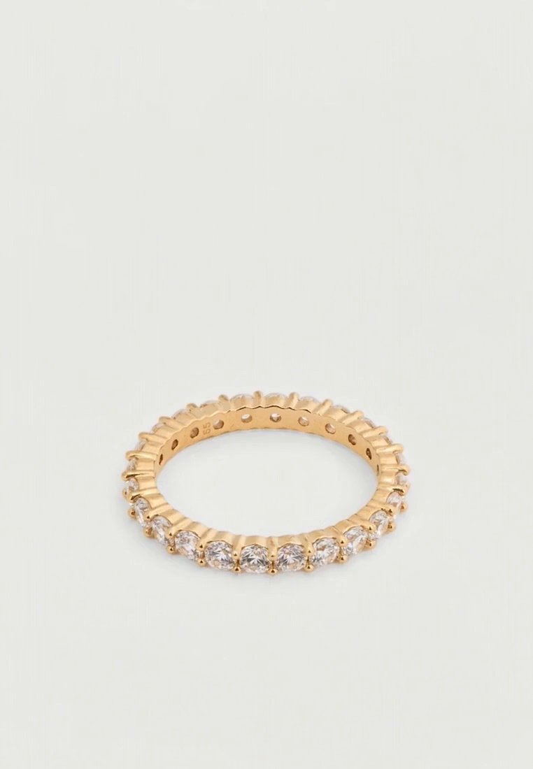 Une bague en or ornée d’une rangée continue de pierres précieuses transparentes repose sur une surface claire.