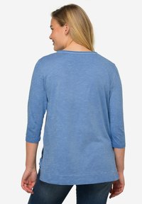 Blusa di cotone blu con maniche tre quarti, scollo rotondo, aperture laterali e un aspetto texturizzato. Tessuto morbido con una vestibilità rilassata.
