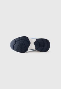Suola di un sneaker blu e bianco che mostra un battistrada texturizzato con le iniziali del marchio e modelli di presa curvi su uno sfondo semplice.