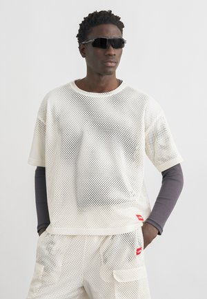 Young man wearing white mesh short-sleeve top and shorts over a long-sleeve dark gray shirt, with black futuristic sunglasses.