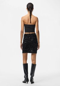 Moteris su ilgais nusiūtomis plaukais, vilkinti juodą kamšą be rankovių, juodą blizgučių mini sijoną ir juodas iki kelių batus, matoma iš užnugario.