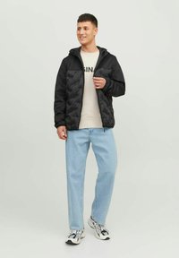 Zwarte gewatteerde jas met een capuchon, contrasterende gladde mouwen, gedragen over een licht sweater en gecombineerd met lichtblauwe jeans en sneakers.