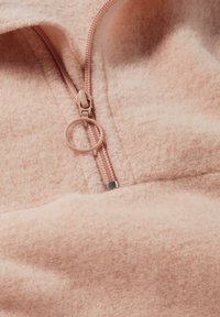 Weiches pinkes Fleece-Pullover mit einem halben Reißverschluss, ausgestattet mit einem Metallreißverschluss-Zipper und einer glatten, strukturierten Stoffoberfläche.