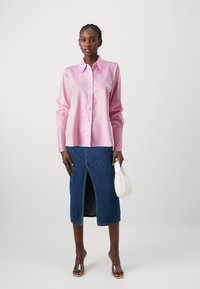 Lyse pink satin skjorte med knapper og lange ærmer; parret med en mørk denim blyantskørt med en frontslids. Klare hæle sandaler og en hvid taske.