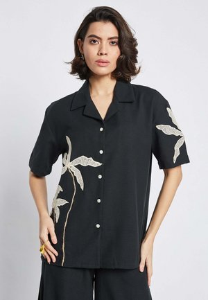 Black short-sleeve shirt made of soft fabric, featuring cream floral embroidery, round collar, and button-up front.