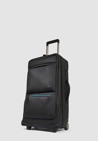 Maleta negra con ruedas, acabado mate y suave, que cuenta con un bolsillo frontal con cremallera con un detalle en color teal, asa retráctil y ruedas duraderas.