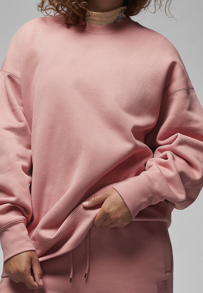 Sweatshirt rose en tissu doux, avec une coupe décontractée et des épaules tombantes. Détails notables : poignets côtelés et ourlet avec cordon de serrage.
