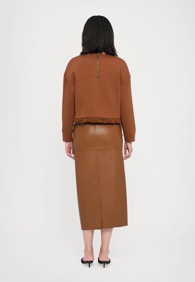 Hnědý zkrácený svetr s volánovým lemováním, má zip na zadní straně. Spárován s těsně přiléhající hnědou koženou sukní, hladký materiál.