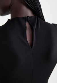 Close-up of a person wearing a black garment with a keyhole button closure at the back neckline and braided hair pulled to one side.