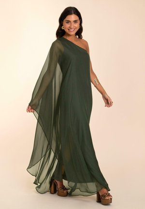 Vestido de gasa en verde oscuro, con un diseño de un solo hombro y una tela fluida. Combinado con tacones de plataforma gruesos, que destacan por su textura suave y drapeado.