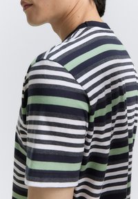 Gestreiftes T-Shirt mit navy, weiß und grünen Streifen. Baumwollmaterial, runder Halsausschnitt, kurze Ärmel und eine lässige Passform. Sichtbare Nahtdetails.