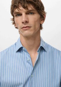 Svjetlo modra srajca s gumbi in klasično ovratnikom, z kontrastnimi belimi črtami in mehko teksturo.