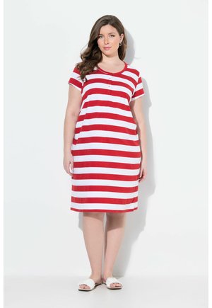 Femme portant une robe courte à manches courtes rayée horizontale rouge et blanche jusqu'aux genoux avec des boutons, debout devant un fond blanc en sandales blanches.