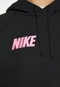 Svart hoodie med rosa "NIKE"-logotyp, dragsnören vid halsringningen och mjukt tyg med textur. Framhävda sömdetaljer.