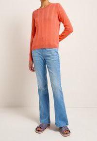 Coral ribbed sweater with long sleeves paired with light blue flared jeans. Footwear features purple slide sandals with a multi-band design.