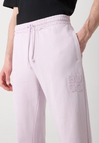 Lyse lilla sweatpants med elastisk talje og snor. Har sidelommer og broderet "HUGO" logo. Glat tekstur.