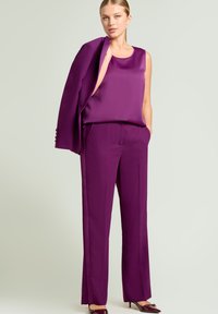 Paars satijnen mouwloze top gecombineerd met bijpassende op maat gemaakte broek met een ontspannen pasvorm en zijzakken, aangevuld met een gestructureerde blazer.