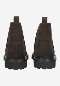 Brązowe botki zamszowe z elastycznymi panelami po bokach, grubą czarną gumową podeszwą i pętelkami ułatwiającymi zakładanie. Widok od tyłu ukazujący detale szwów.