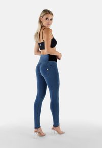 Jeans blu a vita alta con una texture liscia, tasche posteriori e cuciture a contrasto. Indossati con un crop top nero e tacchi trasparenti.