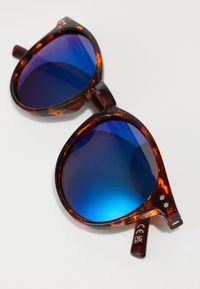 Tortoiseshell sunglasses with oversized blue gradient lenses. Rounded frames, smooth texture, and metal accents on the temples.