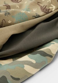 Trois morceaux de tissu pliés : un beige avec des motifs bleus et bruns, un vert foncé, et un beige avec un motif camouflage vert.
