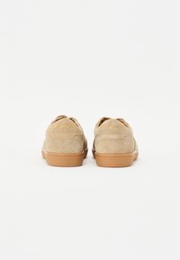 Sneaker in suede tan con una texture liscia, suole in gomma e lettering dorato sul retro. Forma arrotondata, design low top e chiusura con lacci.
