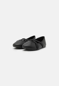 Bailarinas negras hechas de material suave, con un perfil bajo, tiras elásticas cruzadas y punteras redondeadas para un diseño sencillo.