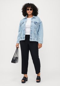 Giacca di jeans azzurro chiaro con due tasche sul petto, t-shirt bianca, pantaloni neri rilassati, borsa nera testurizzata e scarpe slip-on nere spesse.