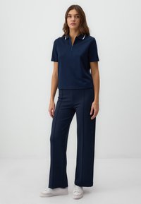 Navy polo shirt with short sleeves and zipper, paired with wide-leg navy pants featuring vertical seams, worn with white sneakers.