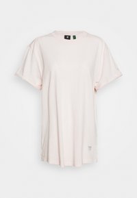 Jasnoróżowa, oversize, krótko rękawek koszulka T-shirt z dekoltem okrągłym i małą metką przy dolnym brzegu na białym tle.