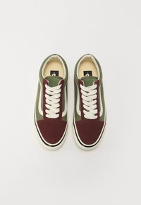 Låga sneakers med en grön kanvasöverdel, burgundy mockadetaljer, vita snören och en krämfärgad gummisula med svarta ränder.