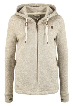 Beige strikket hettegenser med glidelås foran, snorhette og to sidelommer. Har brune detaljer og tommelhull i mansjettene.