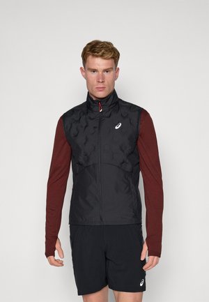 Gilet sans manches noir avec une texture matelassée, col haut et un zip rouge, associé à une chemise à manches longues bordeaux et un short noir.