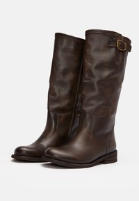 Brown leather knee-high boots with a textured finish, rounded toe, low stacked heel, and adjustable buckle detail on the side.