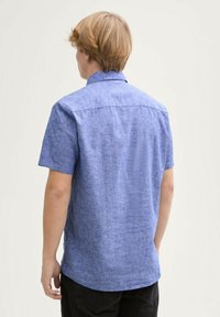 Cămașă cu mânecă scurtă dintr-un material bleu deschis cu un finisaj texturat, guler clasic și tiv curbat. Vedere din spate care arată cusăturile umerilor și fără imprimeuri vizibile.