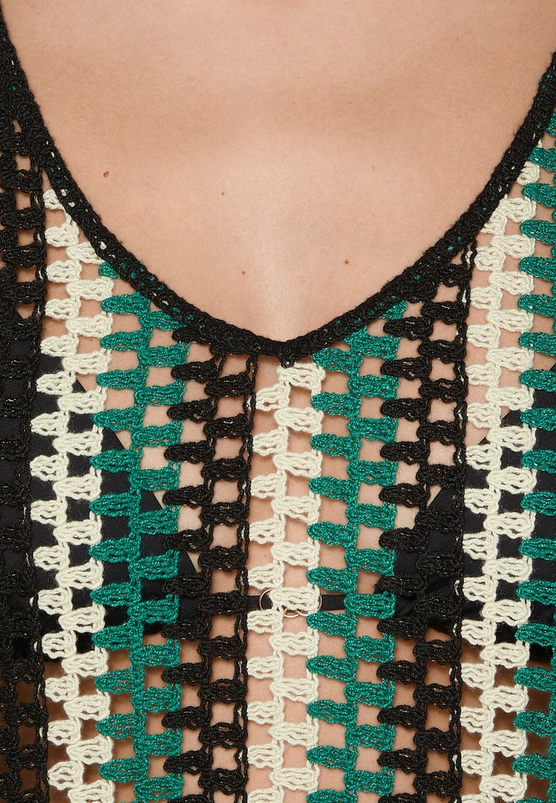 Top de ganchillo con escote en V, con un patrón de colores negro, verde y crema en un diseño de malla. Tejido texturizado con punto abierto.