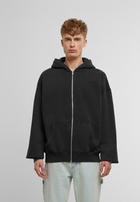 Črn zip-up bombažni hoodie z oblačilom na vrvico, velikimi sprednjimi žepi in sproščenim krojem. Gladka tekstura z minimalnim detajliranjem.