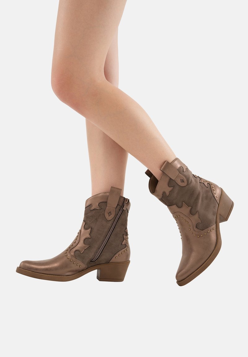Botas de tobillo marrones de cuero, con diseño en relieve de hojas, tachuelas decorativas y cremallera lateral. El tacón grueso proporciona estabilidad y altura.