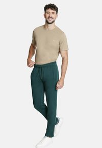 Camiseta corta de manga corta color marrón con un pequeño logo y pantalones jogger verde oscuro con cintura elástica, combinados con zapatillas blancas.