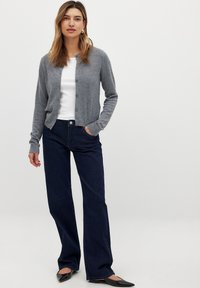 Cárdigan gris de punto con cuello redondo y cierre de botones, combinado con jeans de campana azul oscuro y bailarinas negras con punta.