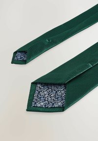 Cravat texturată verde cu un interior patterned de culoare albastru închis, având modele florale albe, cu vârfuri ascuțite și detalii subtile de cusătură.